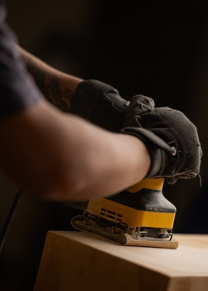Detailed view of a craftsman sanding wood with an electric sander in a workshop.